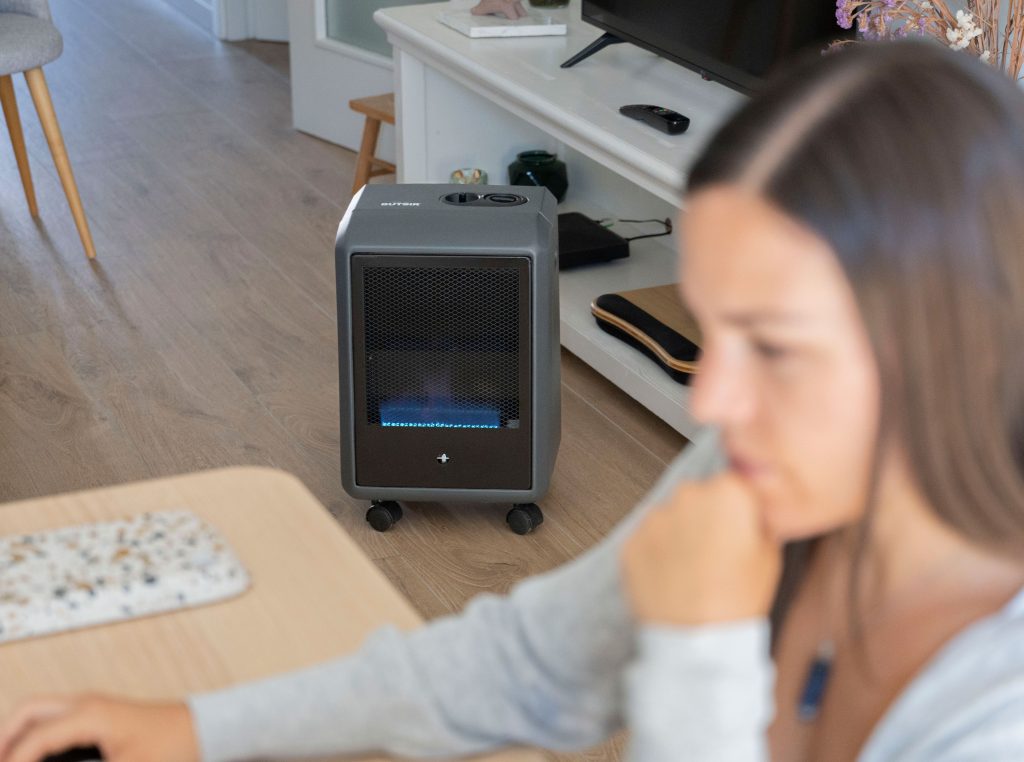 Chica en primer plano algo borrosa en una mesa de trabajo con estufa de llama azul BUTSIR al fondo, encendida.